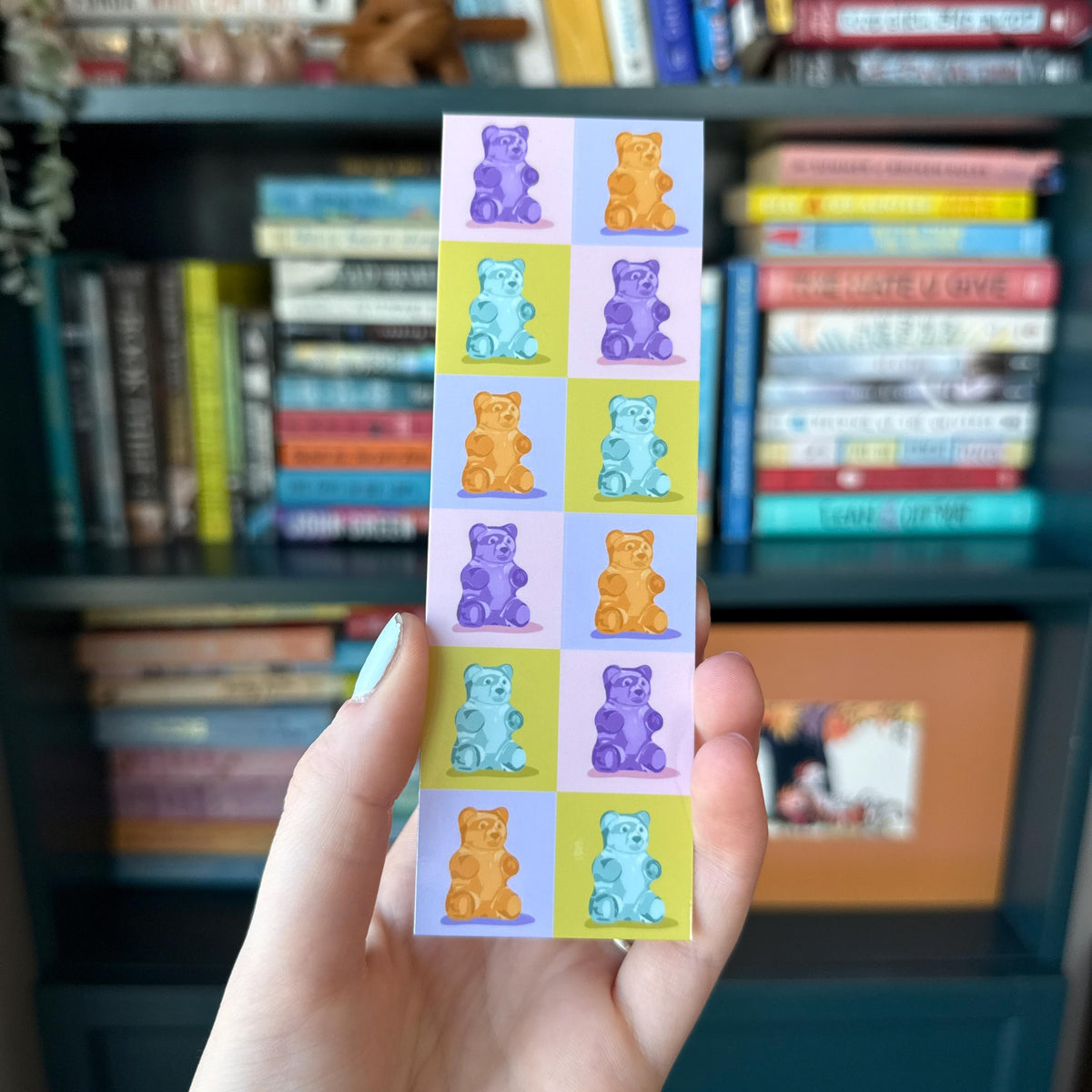 Bookmark featuring a grid of colorful gummy bears, with a blurred bookshelf in the background.