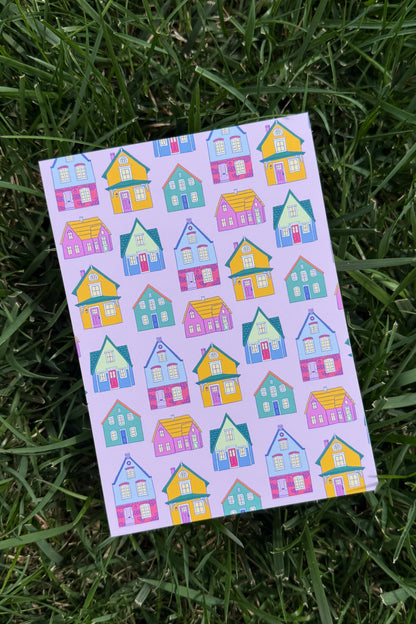 A rectangular art print with a repeating pattern of colorful cartoon houses, placed on green grass.