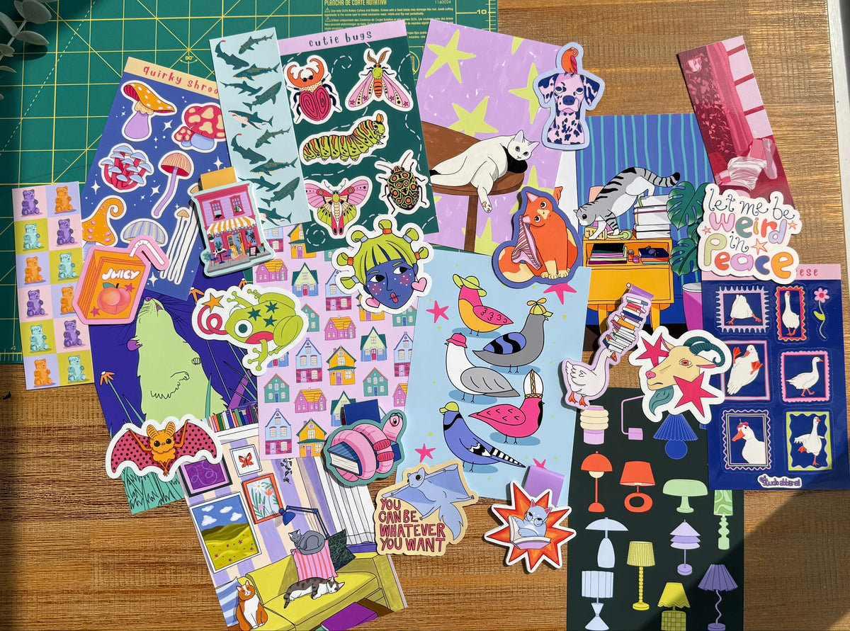 A collection of quirky and colorful stickers stationary arranged on a wooden surface next to a green cutting mat and a window.