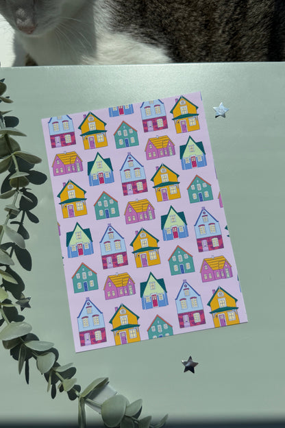 Pink art print featuring colorful whimsical houses on a green surface with a cat visible at the top.